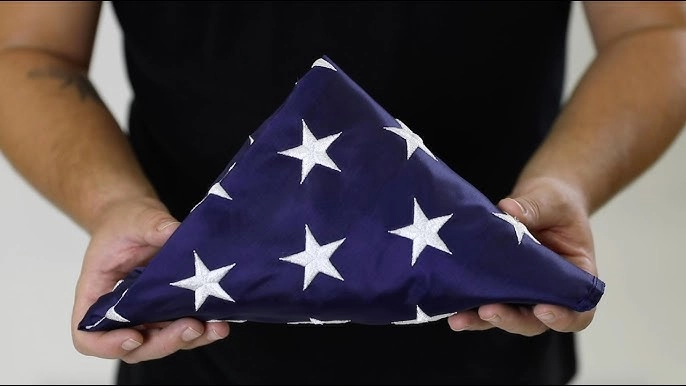 Person holding a properly folded American flag with embroidered stars, symbolizing respect and honor for the flag.